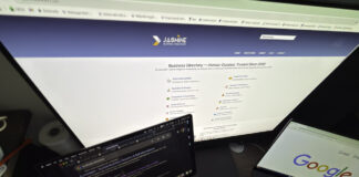 Overhead view of a multi-screen computer workspace with laptop and monitor displaying business directory websites, illustrating the digital research process for finding professional services.
